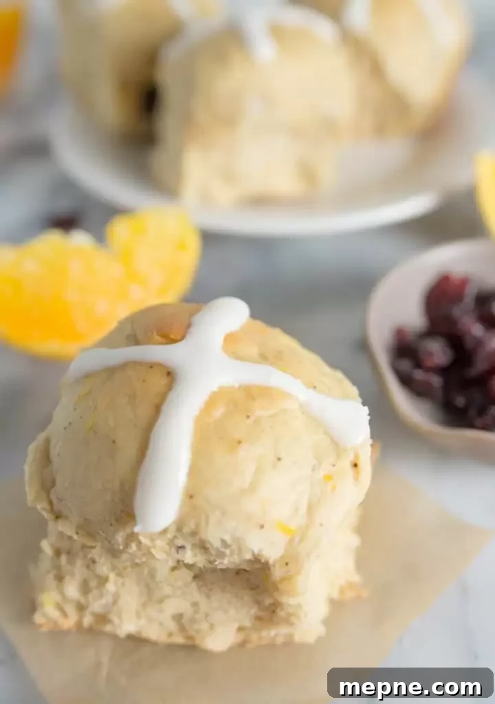 Cranberry Orange Hot Cross Buns Recipe 6 hot cross bun with cranberries, an orange slice, and more cranberry orange hot cross buns in the background