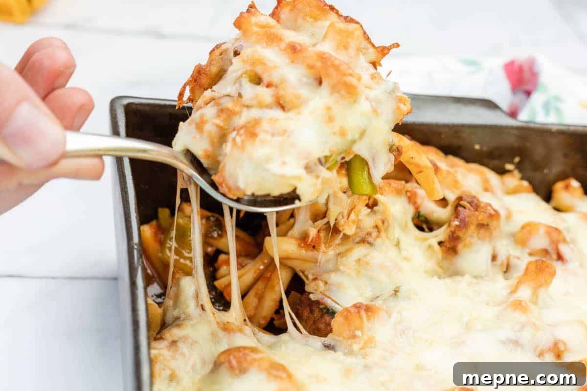 35 Classic Casserole Recipes That Have Everyone Coming Back 2 A hand lifts a serving of meatball casserole from a rectangular baking dish, showing melted cheese stretching.