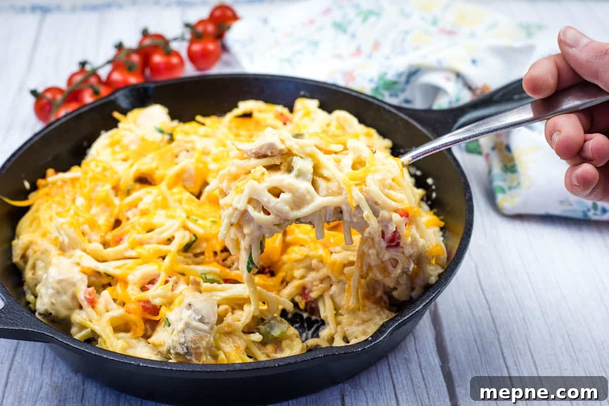 35 Classic Casserole Recipes That Have Everyone Coming Back 16 A hand holding a fork with a serving of chicken spaghetti from a cast-iron skillet.