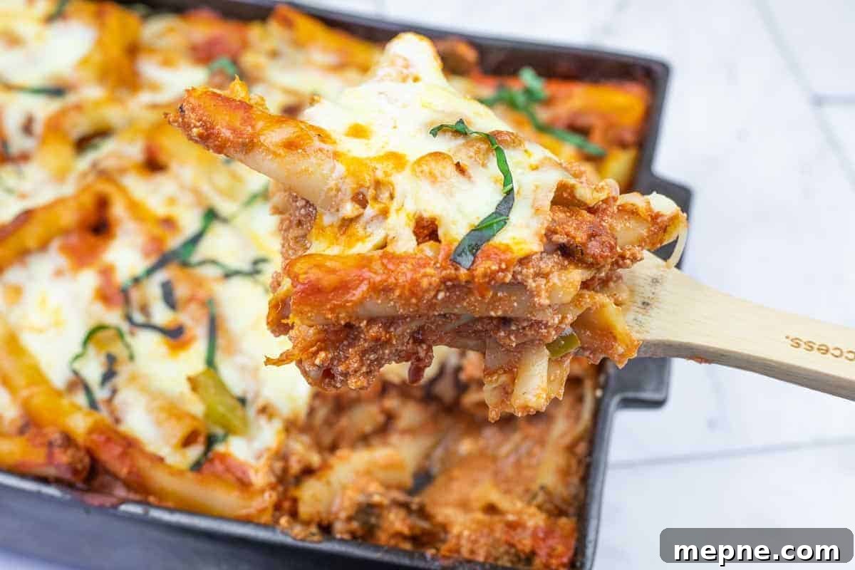 35 Classic Casserole Recipes That Have Everyone Coming Back 4 A close-up of a wooden spoon lifting a serving of baked ziti with melted cheese and tomato sauce from a casserole dish.
