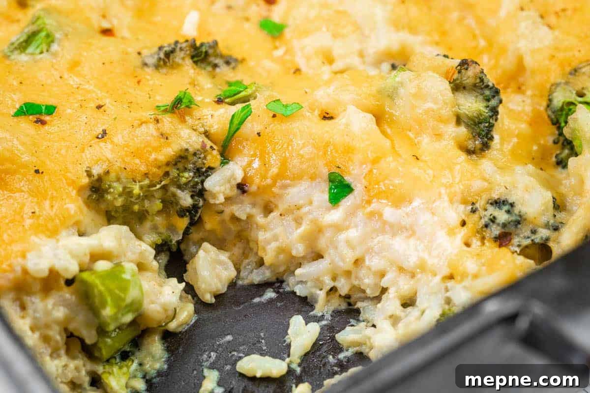 35 Classic Casserole Recipes That Have Everyone Coming Back 5 Close-up of a cheesy broccoli and rice casserole in a baking dish, with a serving removed, showing melted cheese, rice, broccoli, and garnished parsley.