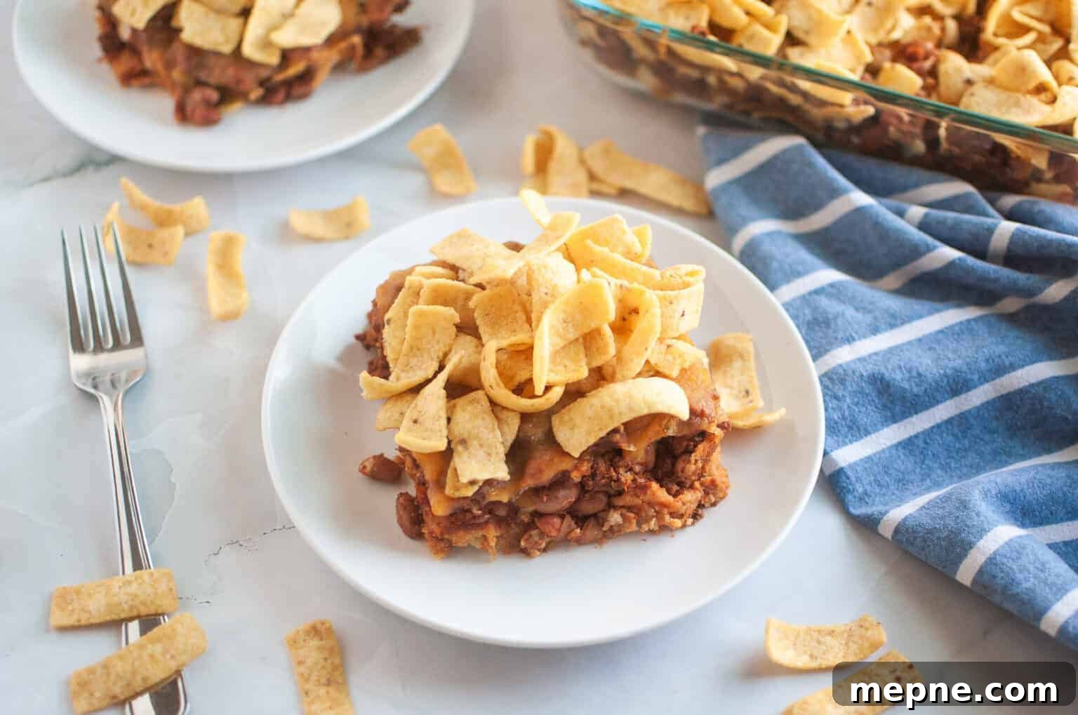 35 Classic Casserole Recipes That Have Everyone Coming Back 8 A white plate with a serving of Frito pie, topped with corn chips, is shown on a light surface.