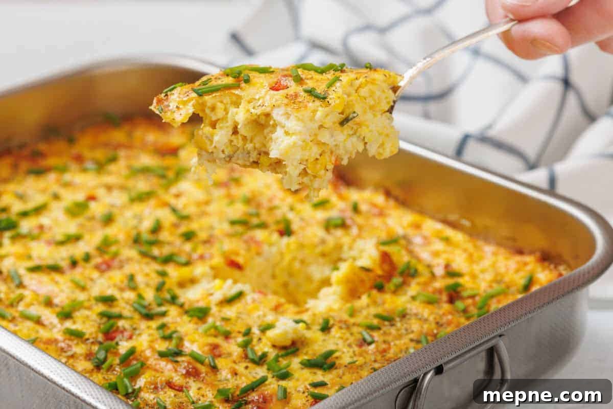 35 Classic Casserole Recipes That Have Everyone Coming Back 10 A Corn Pudding Casserole topped with chopped chives in a metal baking dish, with a portion being lifted out on a serving spatula.