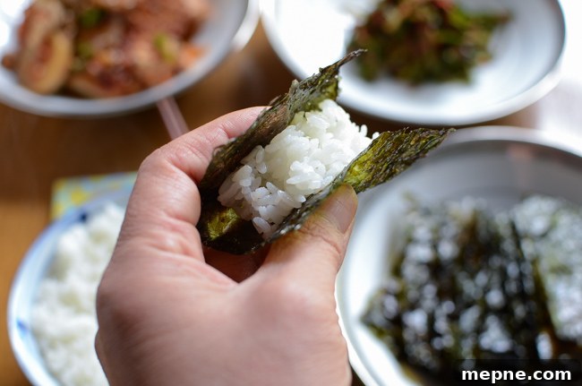 How to Make Crispy Roasted Seaweed Snacks at Home 9 A hand is holding rice wrapped in a piece of roasted seaweed snack.