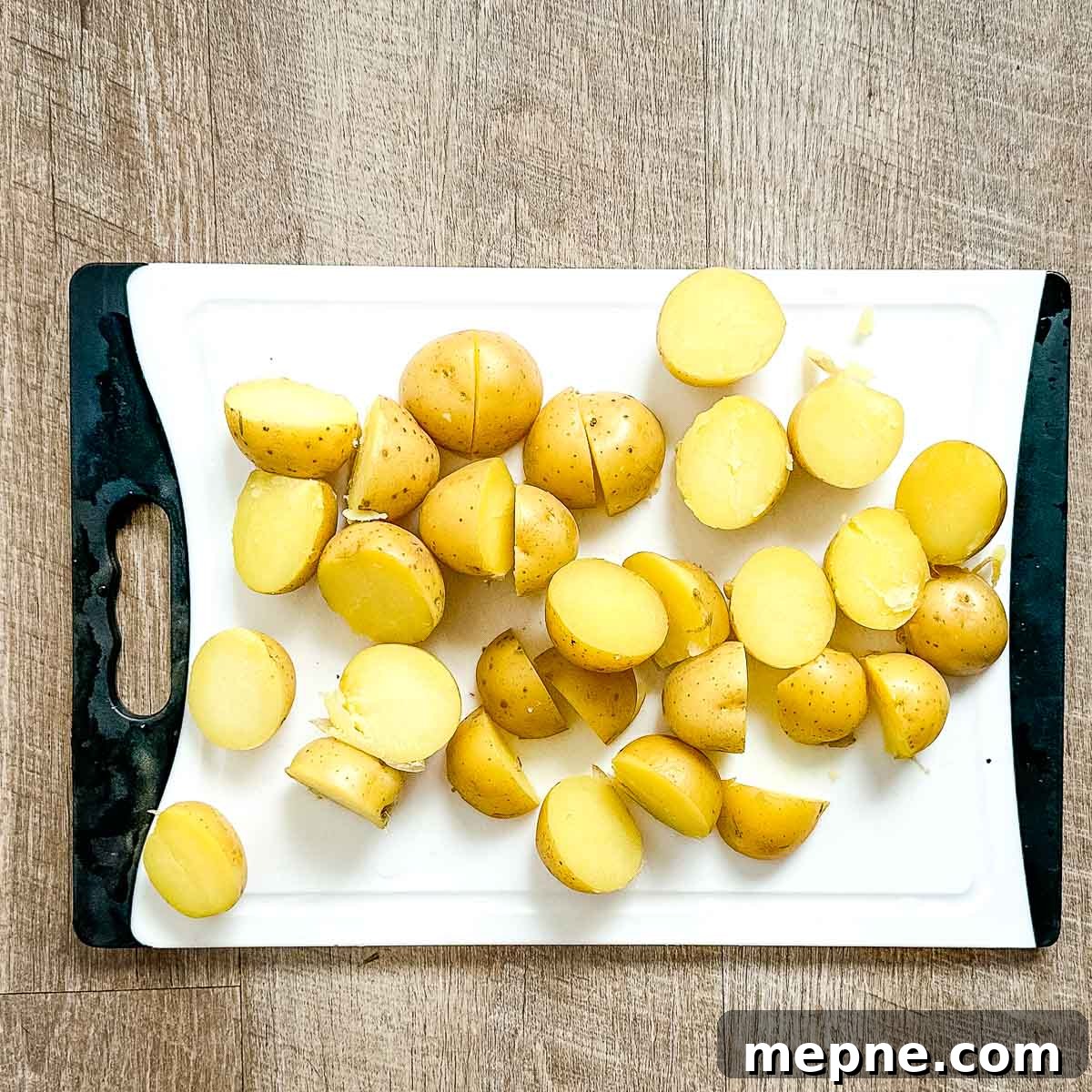Authentic Bavarian Potato Salad with Bacon Recipe 14 cooked, halved yukon gold potatoes on a white cutting board.