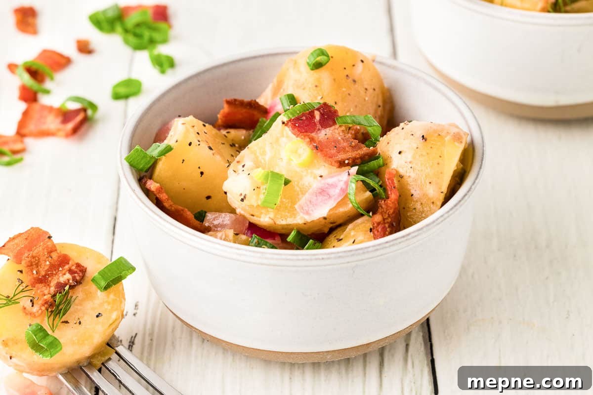Authentic Bavarian Potato Salad with Bacon Recipe 3 A bowl of Bavarian potato salad garnished with chopped green onions and crispy bacon bits on a light-colored wooden surface.