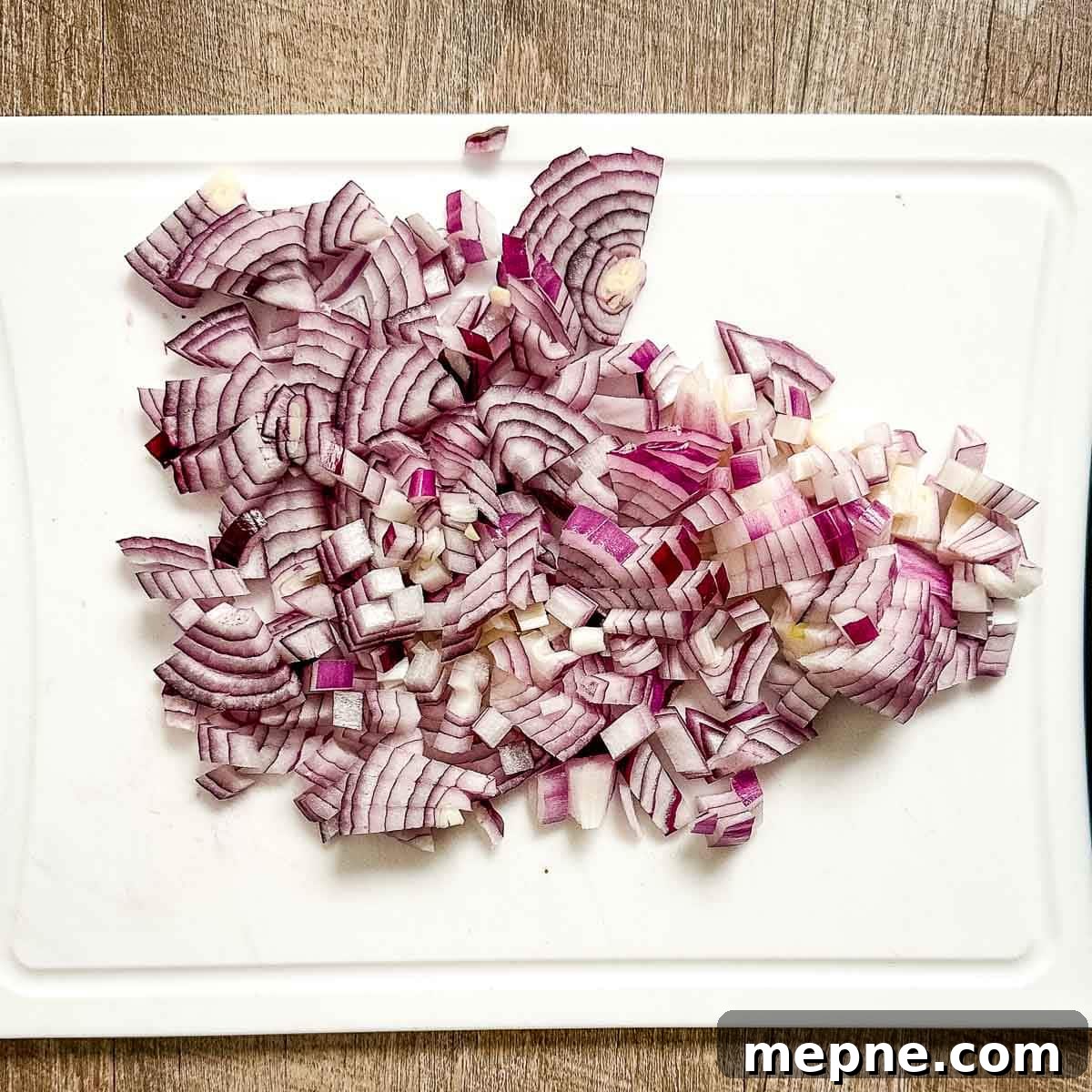 Authentic Bavarian Potato Salad with Bacon Recipe 8 a diced red onion on a white cutting board.