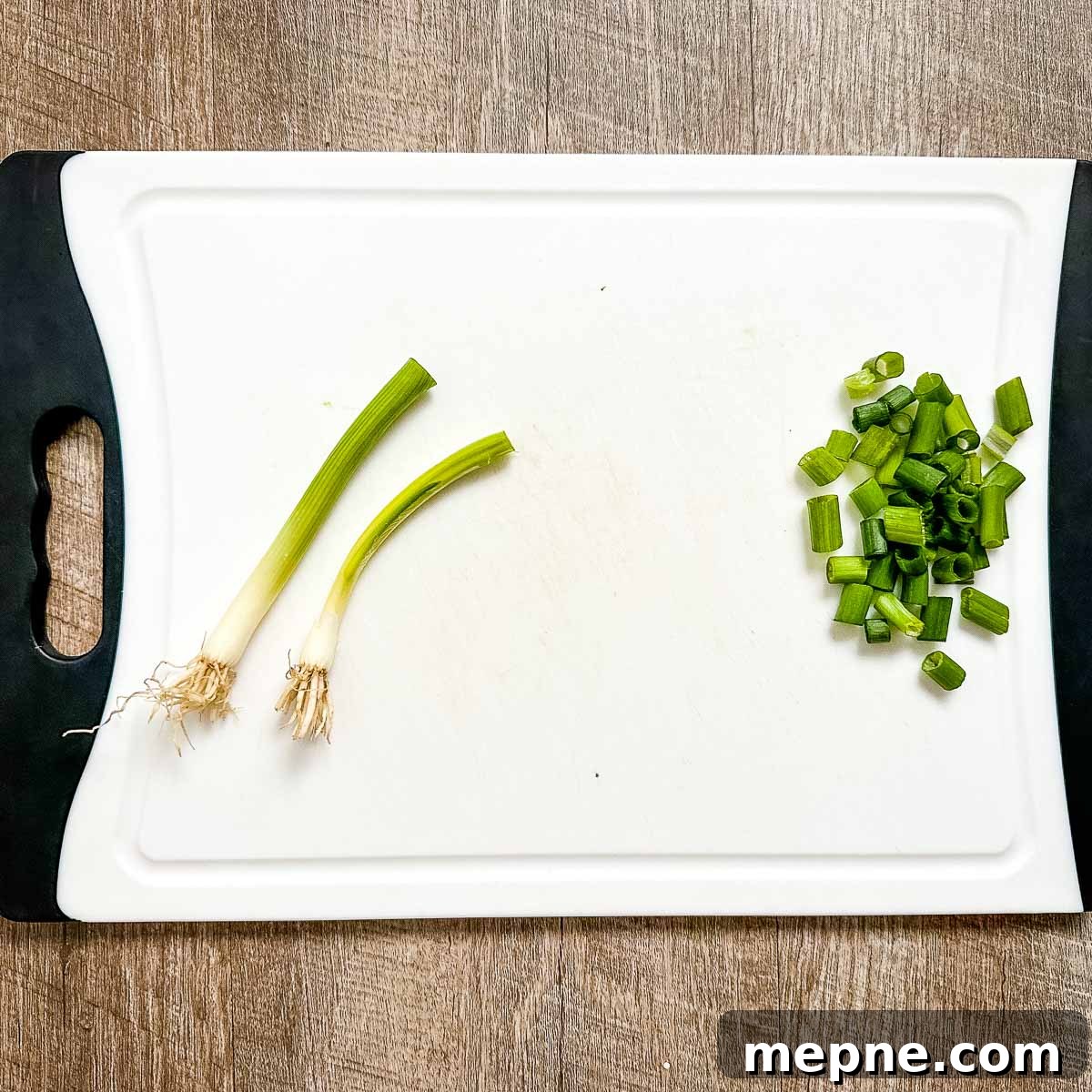 Authentic Bavarian Potato Salad with Bacon Recipe 9 Two scallions are in the process of being chopped on a white cutting board.