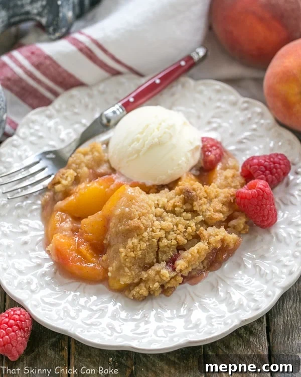 Peach Raspberry Crisp on a white plate topped with a scoop of ice cream.