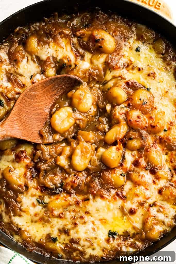 French Onion Gnocchi with Gruyere 6 french onion gnocchi in a skillet with melted gruyere and parmesan cheese and a spoon showing the gnocchi
