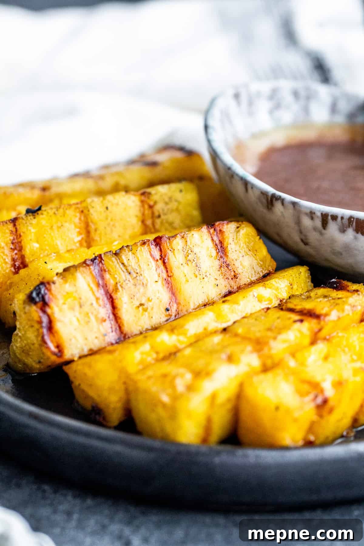 Straight-on shot of pineapple on a plate with sauce.