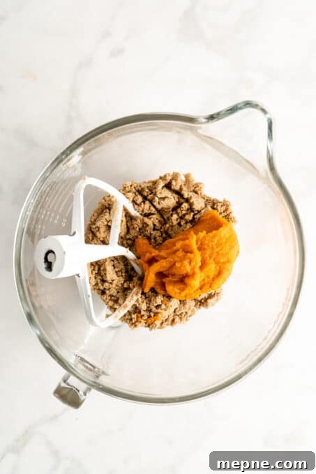 Combine the dough ingredients. Glass mixing dough with pumpkin puree being incorporated into cookie dough