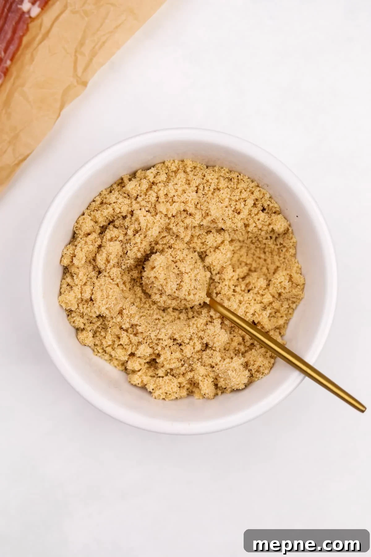 How to Make Candied Bacon: Sweet and Smoky Recipe 5 A small bowl of brown sugar being mixed with a small gold spoon.
