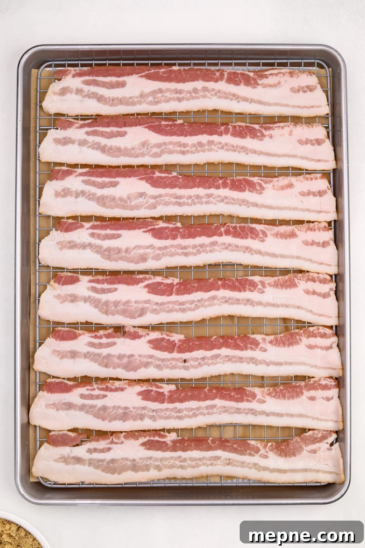 How to Make Candied Bacon: Sweet and Smoky Recipe 6 Raw bacon strips in an even layer on a wire rack set inside of a baking pan.