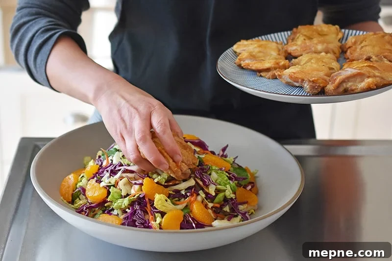 Whole30 Chinese Chicken Salad Gluten Free 11 A person is placing sliced crispy chicken thighs on top of the Whole30 Chinese Chicken Salad