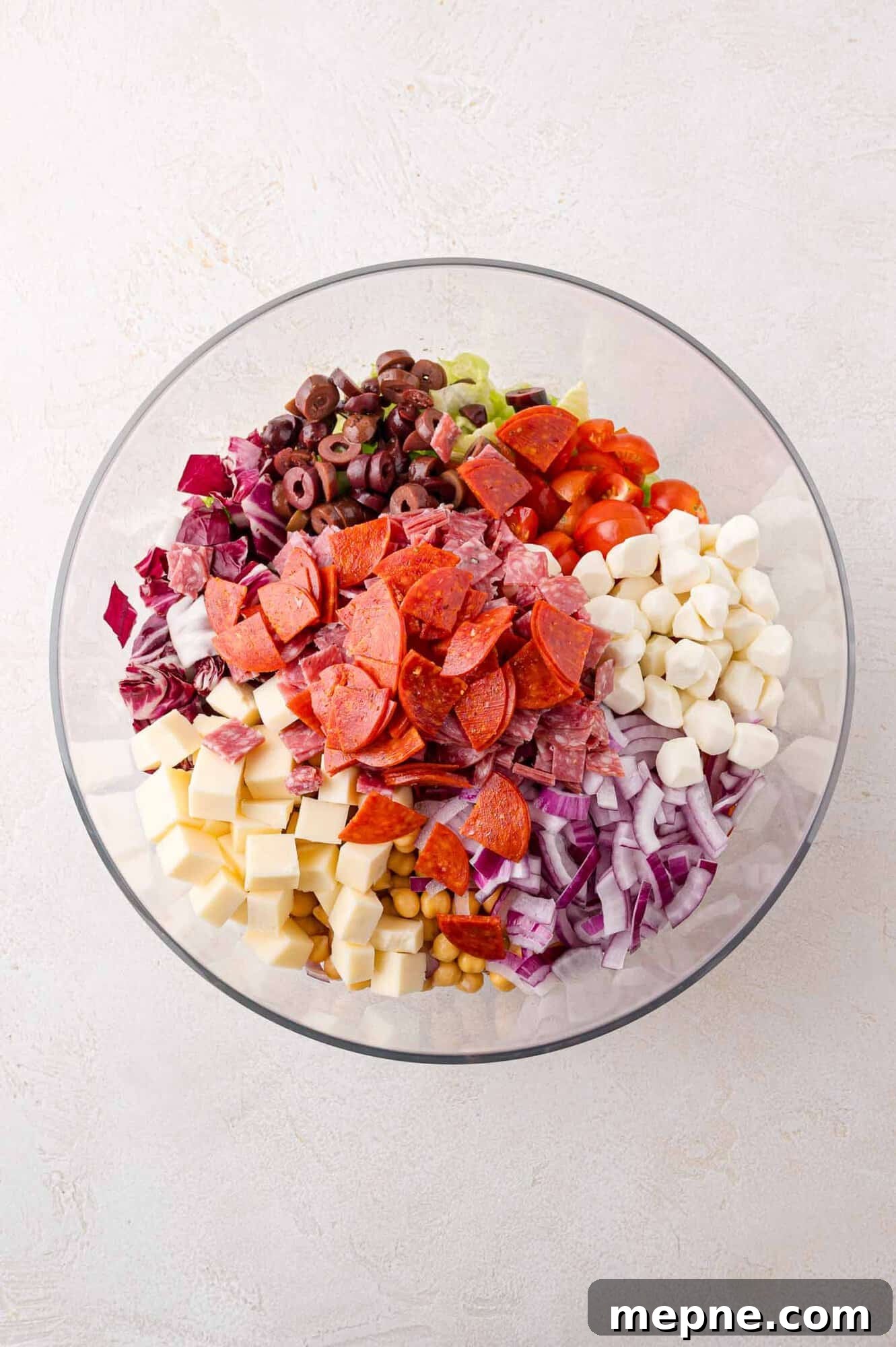 A bowl of assorted chopped salad ingredients including pepperoni, cheese cubes, olives, onions, tomatoes, and mozzarella balls.