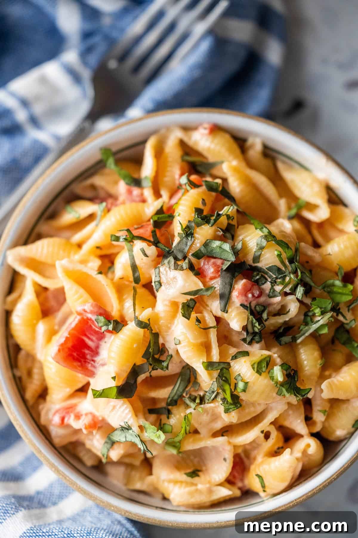 Creamy Tomato Orecchiette Pasta 8 A bowl of creamy tomato pasta with diced tomatoes and chopped basil beside a napkin and fork.