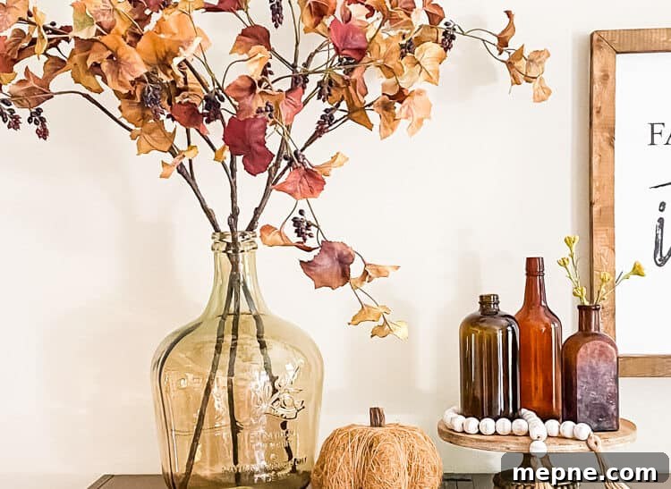 display of glass vase with fall leaves pumpkin and trio of amber vintage glass bottle on top of shelf
