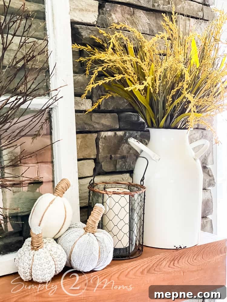 Stacked stone fireplace with antique window frame on wood mantel. Mantle has enamel jug with fall grasses to add fall color and three small sweater pumpkins.