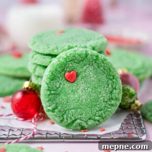 Soft Chewy Grinch Sugar Cookies for Christmas 12 grinch cookie leaning up against a stack of cookies with milk in the background