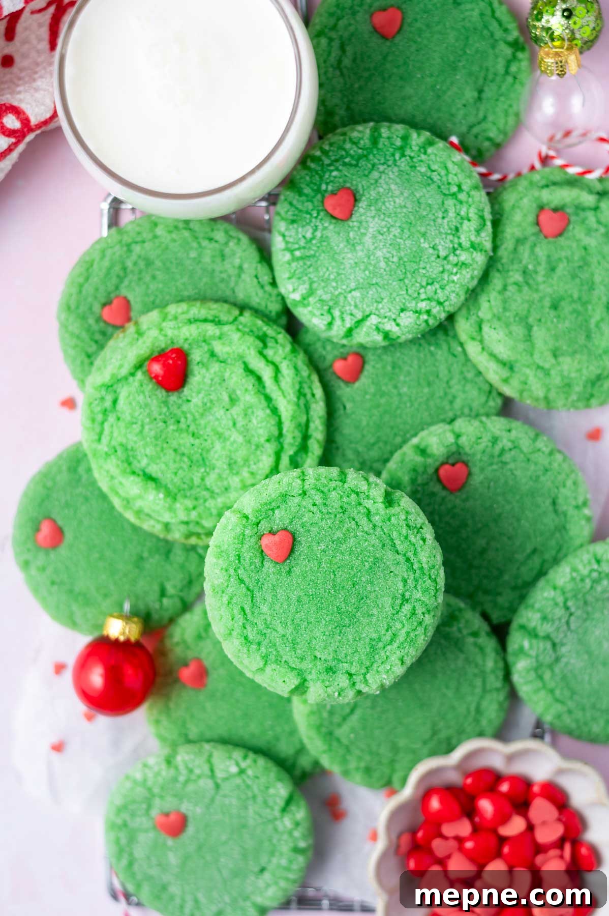 Soft Chewy Grinch Sugar Cookies for Christmas 3 pile of grinch cookies with a glass of milk, bowl of red sprinkles and some ornaments