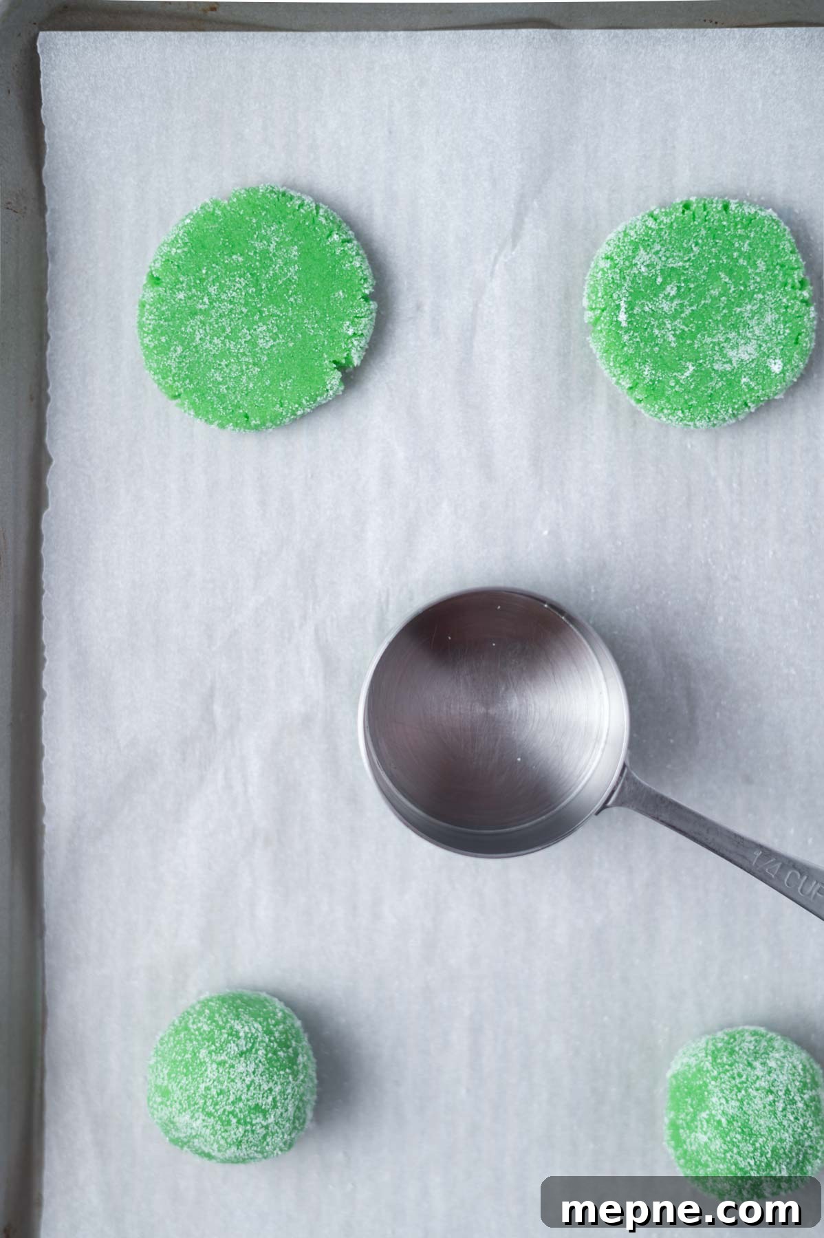 Soft Chewy Grinch Sugar Cookies for Christmas 8 cookie dough on a parchment lined baking sheet with some flattened with a measuring cup