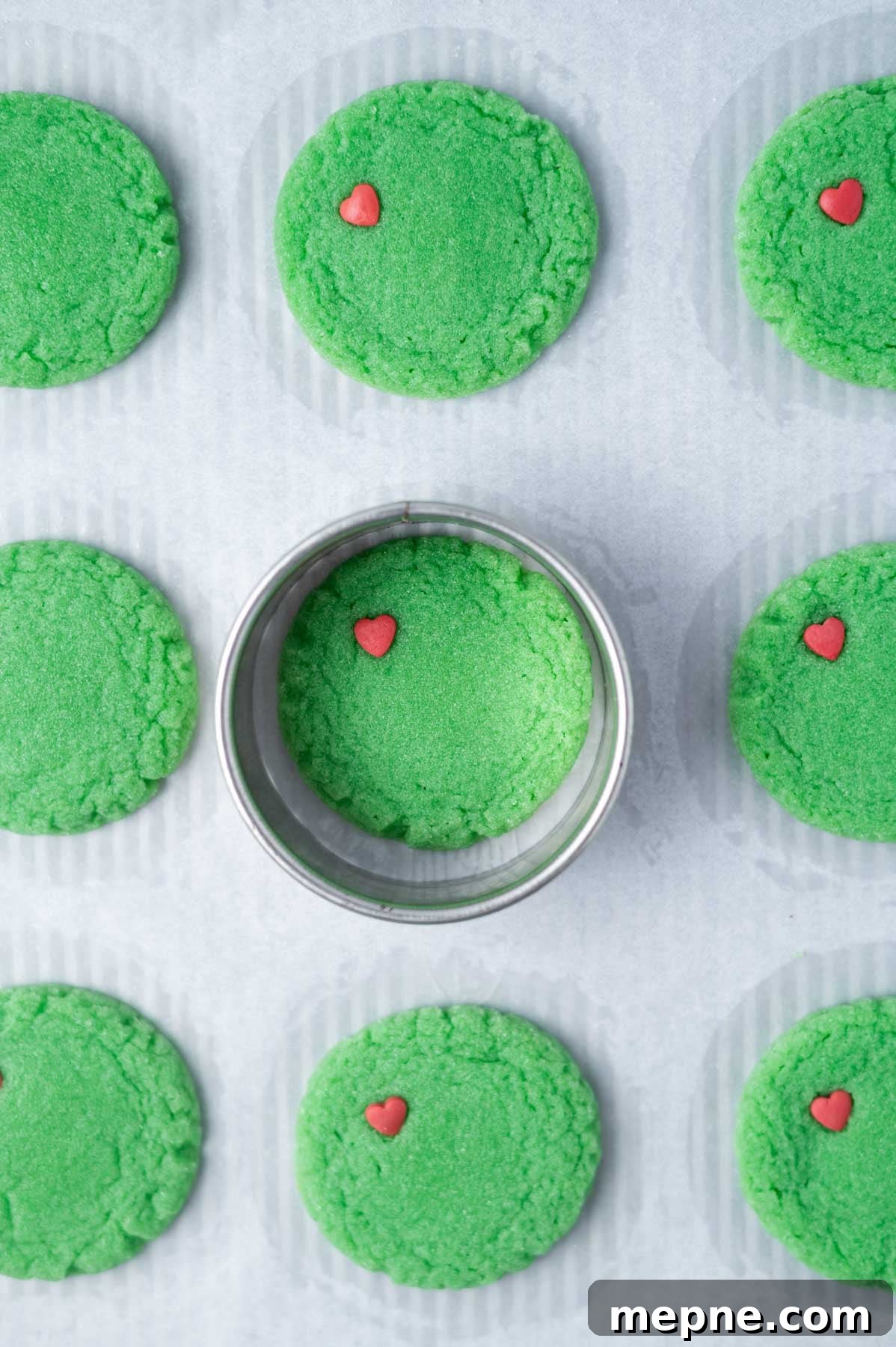 Soft Chewy Grinch Sugar Cookies for Christmas 9 round green baked cookies on a parchment lined baking sheet with a biscuit cutter around one