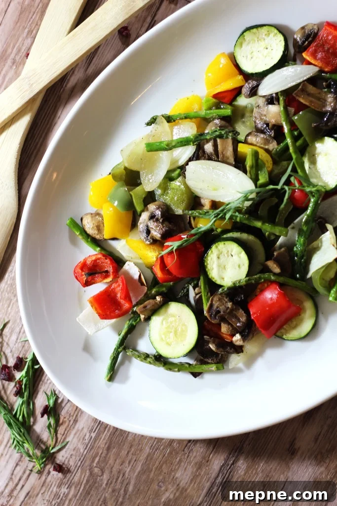 Crispy Oven Roasted Vegetables with Garlic and Herbs 2 A white platter containing a variety of oven roasted vegetables such as asparagus, peppers and mushrooms sitting on a wooden table.