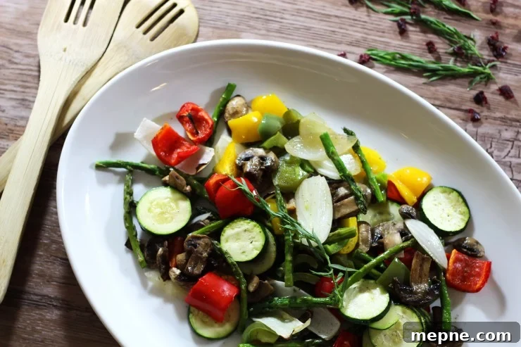 Crispy Oven Roasted Vegetables with Garlic and Herbs 8 A white serving dish containing fresh roasted vegetables sitting on a wooden table, wooden spoons crossed.