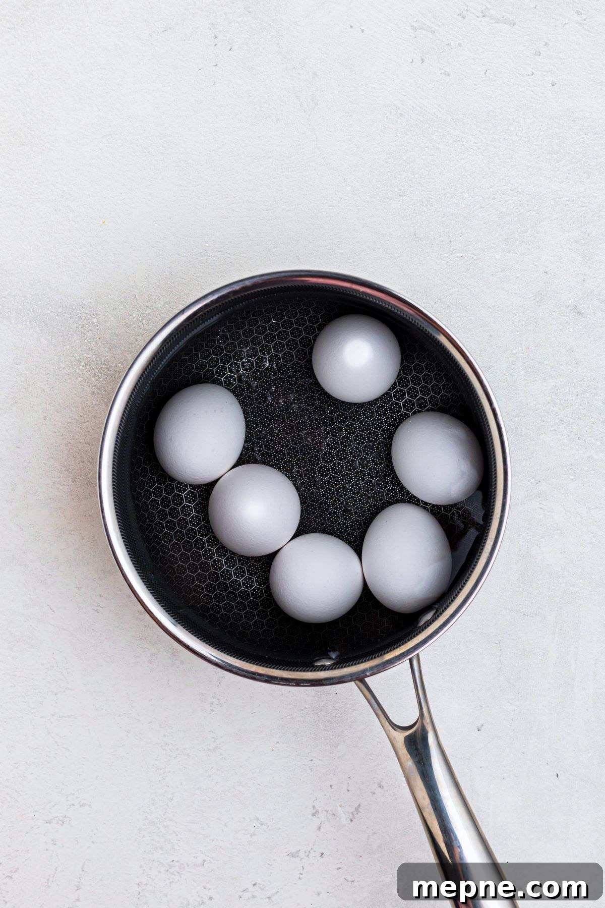 Six whole eggs in shells in a saucepan, covered in water, on a marble table, before boiling. 