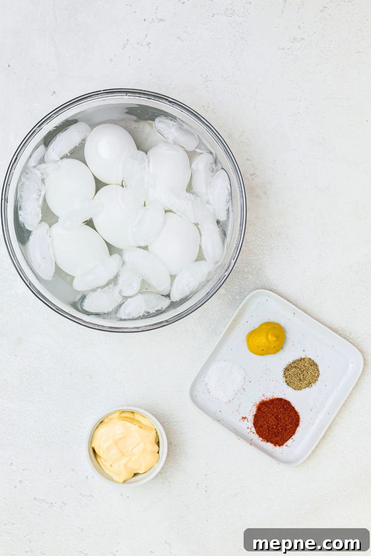 Boiled eggs in a clear glass bowl, filled with water and ice. 