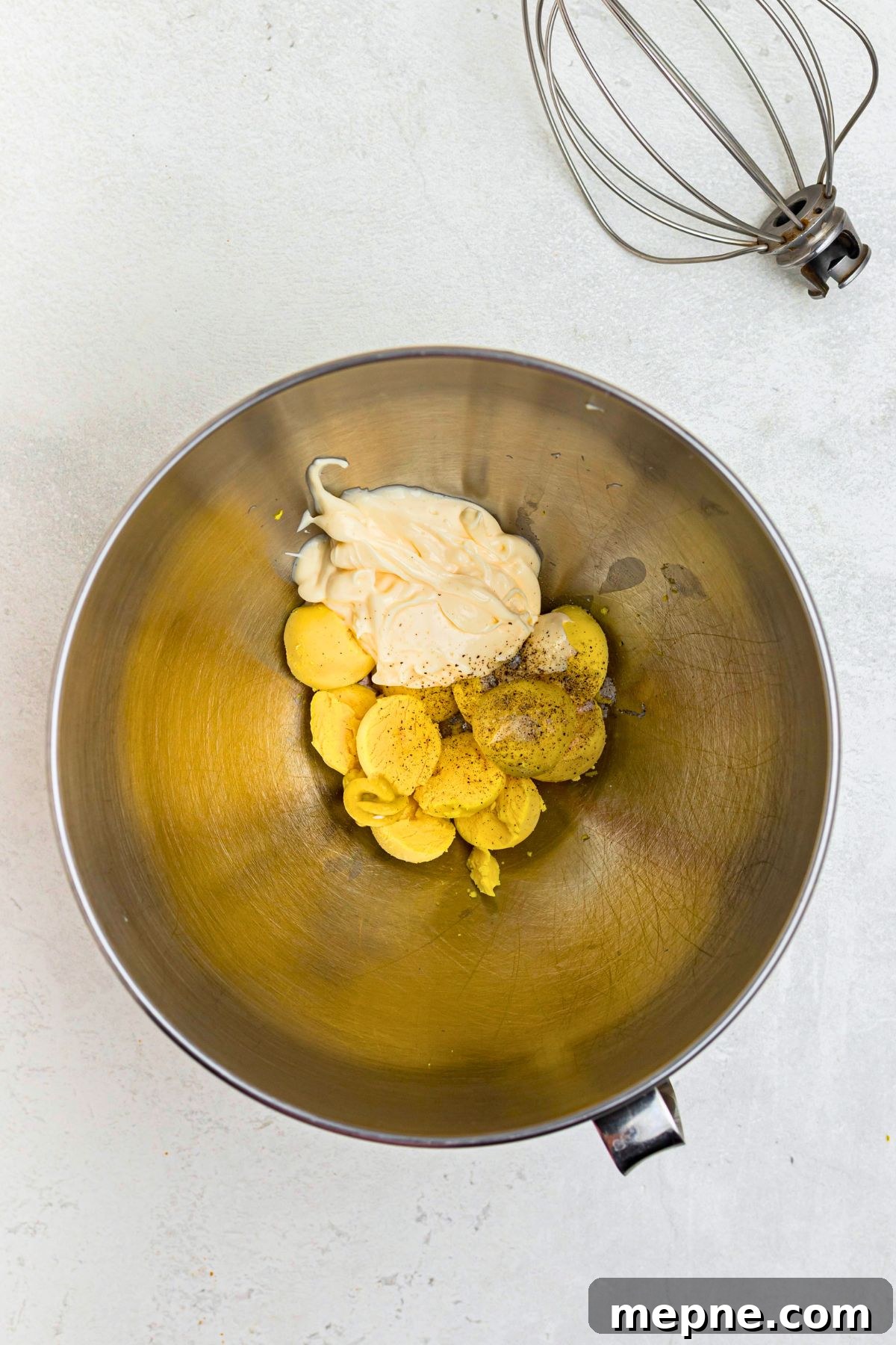 Egg yolks, mustard, mayo, and seasonings, in a silver bowl before mixing.