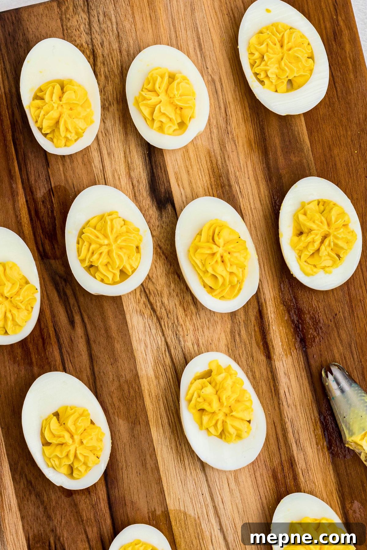 Egg halves piped with yellow yolk mixture to fill center, on a wooden cutting board. 