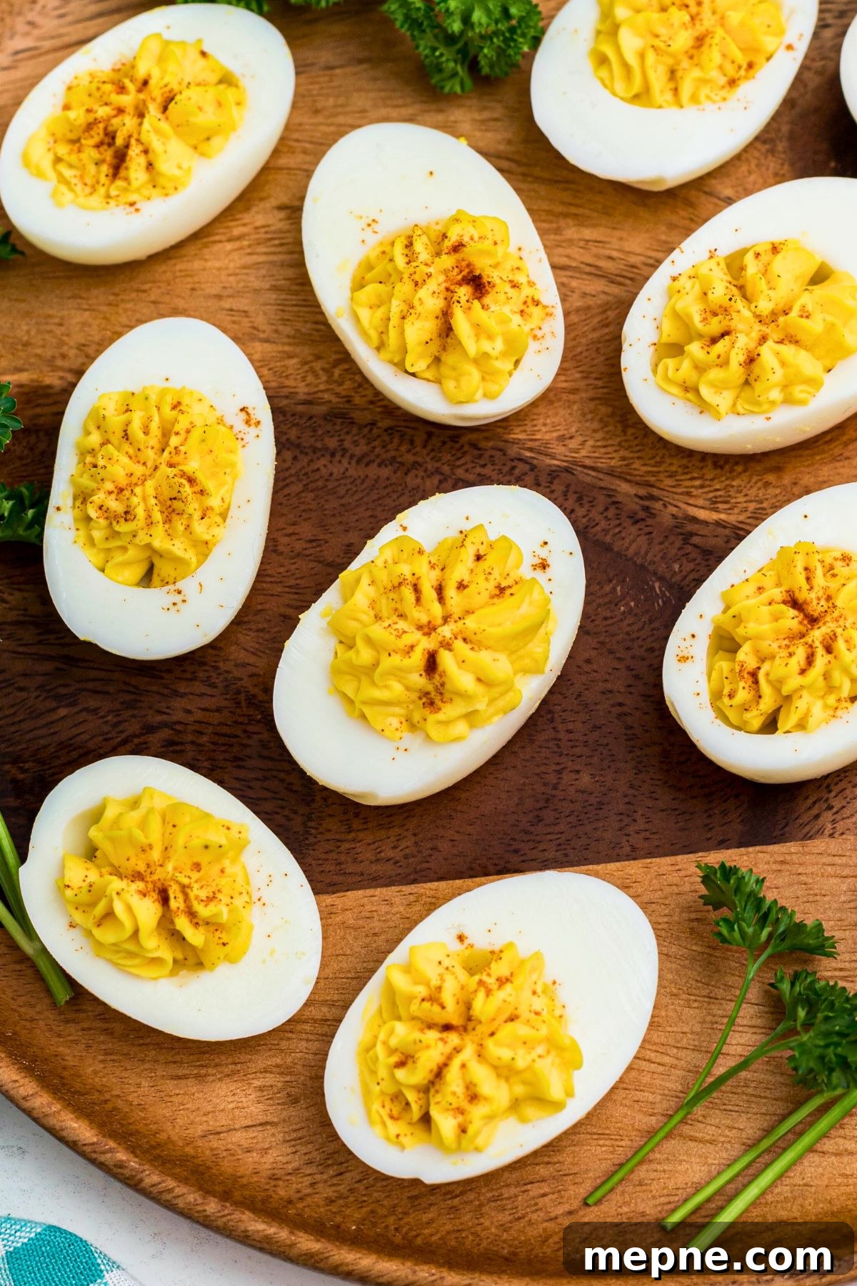 Bright white and yellow deviled eggs, sliced in half, on a round wooden serving platter with parsley garnish.