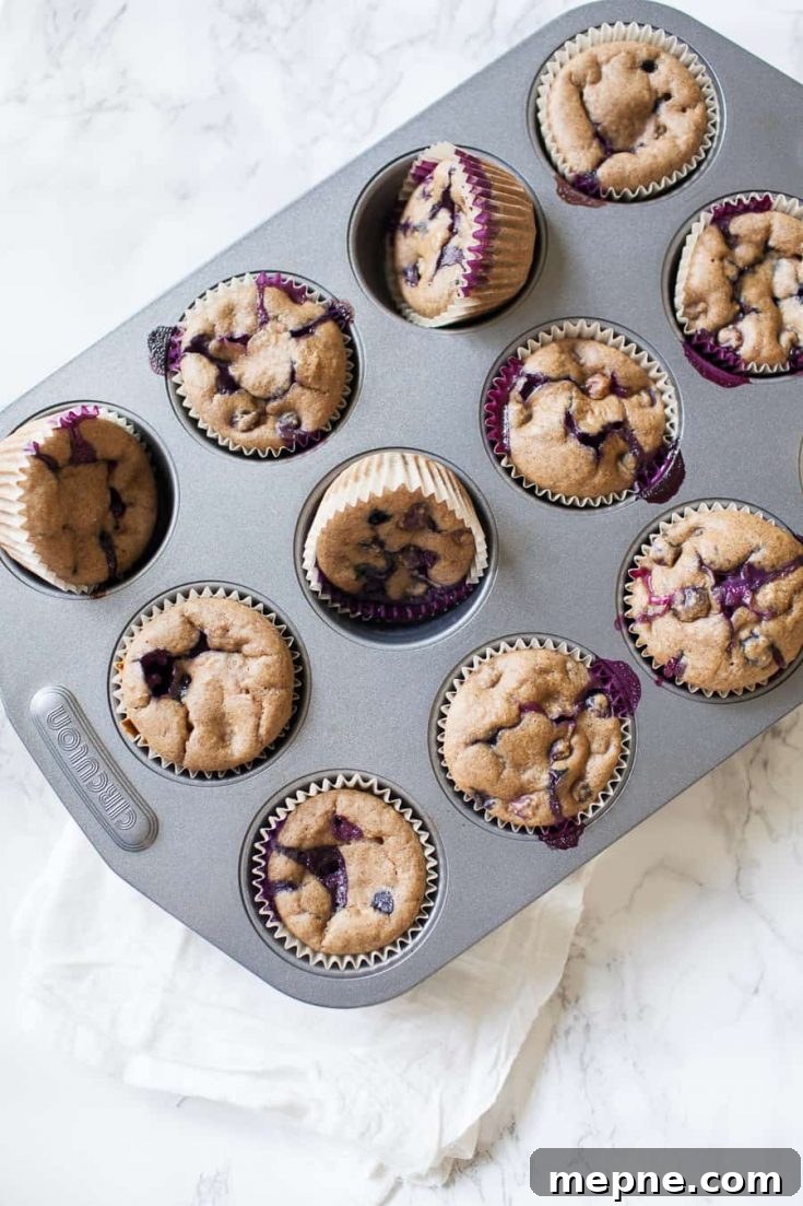 healthy no sugar added blueberry muffins in a silver muffin tin on a white marble countertop 