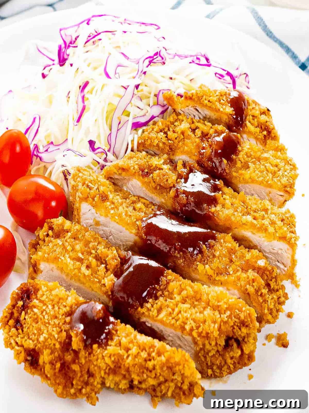Crispy tonkatsu with tonkatsu sauce next to shredded cabbage and tomatoes.