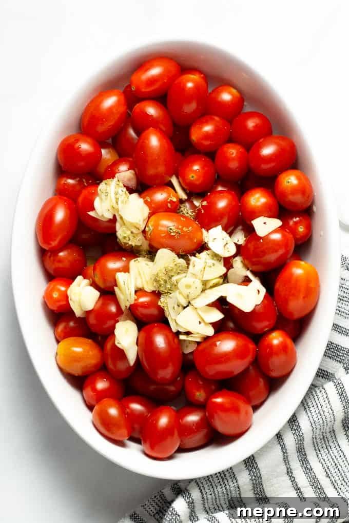 Overhead shot of grape tomatoes topped with sliced garlic, dried oregano and olive oil
