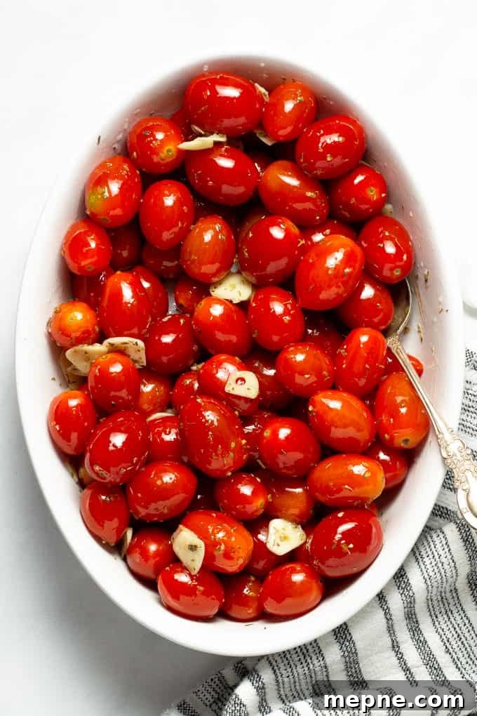 Overhead shot of a white oval baking dish filled with grape tomatoes tossed with olive oil, garlic and oregano