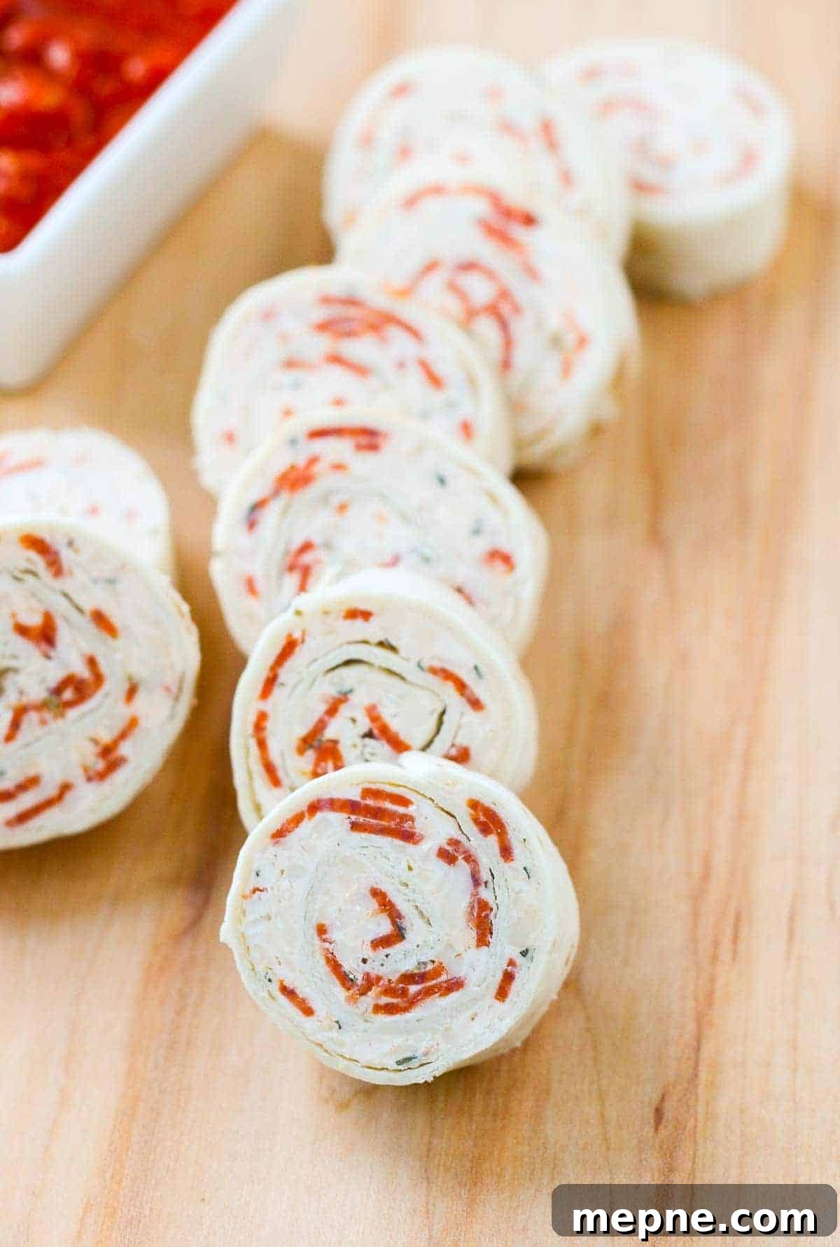 Pepperoni Pizza Tortilla Pinwheels Recipe 2 Pizza tortilla pinwheels arranged on a wooden board.