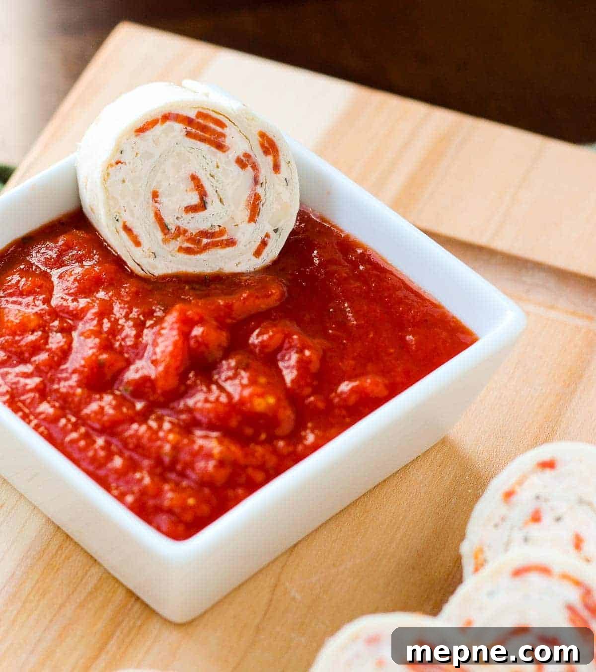 Pepperoni Pizza Tortilla Pinwheels Recipe 3 Pizza tortilla pinwheel being dipped in pizza sauce.