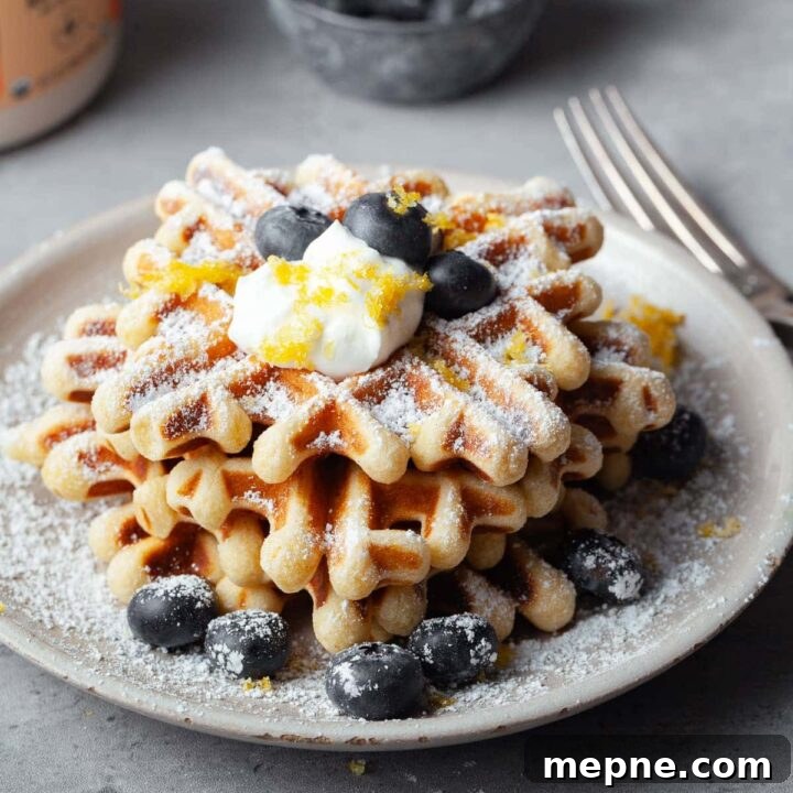 close up of sour cream waffles, gluten free waffles topped with powdered sugar, sour cream and fresh berries