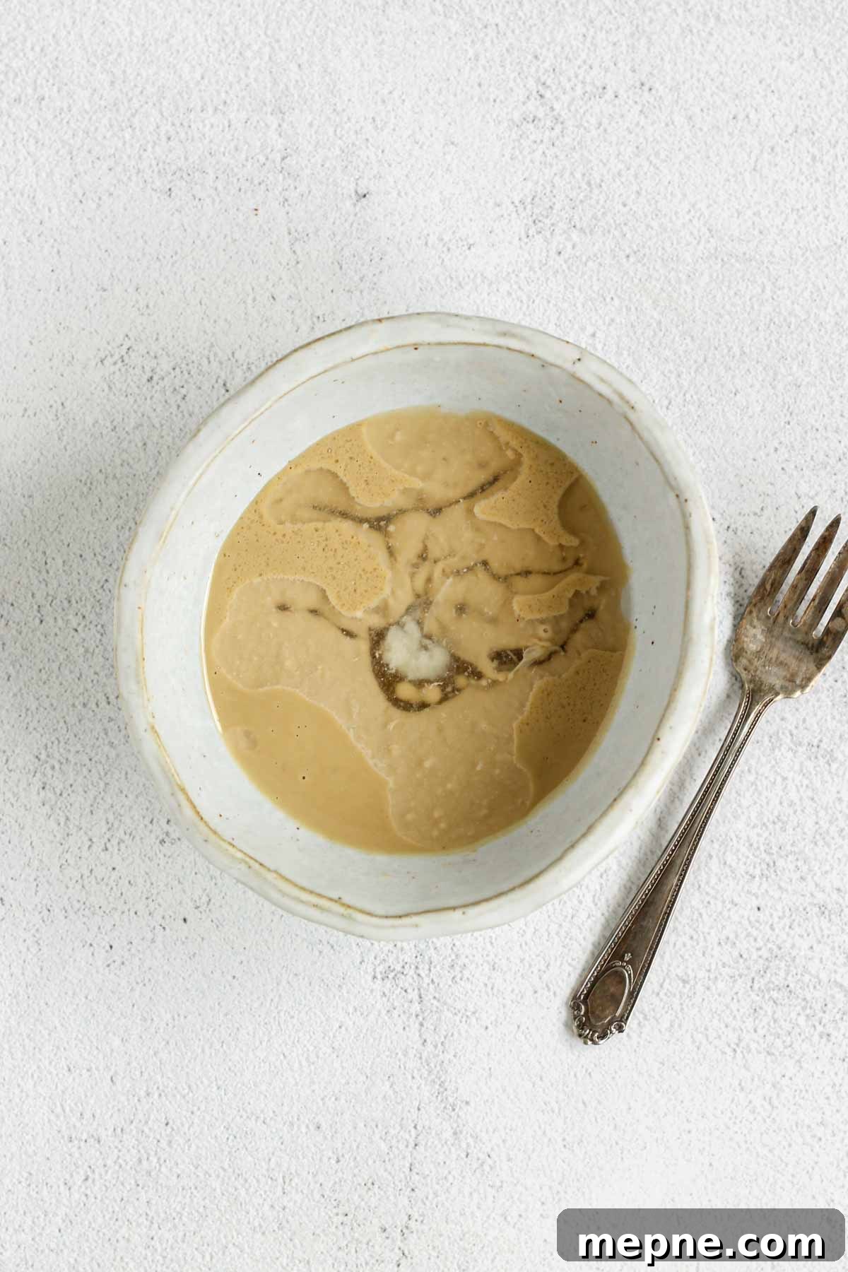 Creamy Maple Tahini Dressing for Salads and Grain Bowls 4 Maple tahini salad dressing ingredients in a shallow bowl unmixed with a fork on the side of the bowl.
