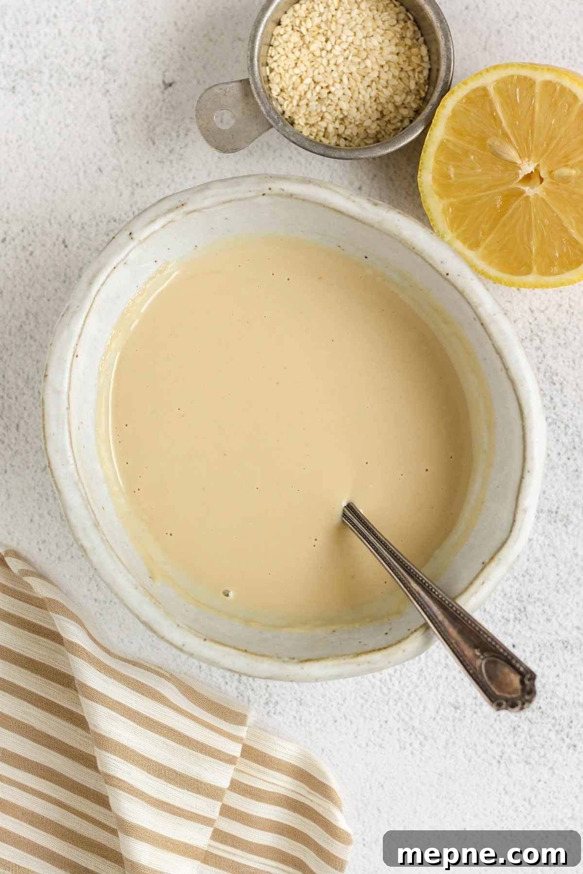 Creamy Maple Tahini Dressing for Salads and Grain Bowls 7 Maple tahini dressing in a shallow bowl with a dish of sesame seeds and half a lemon on the side.