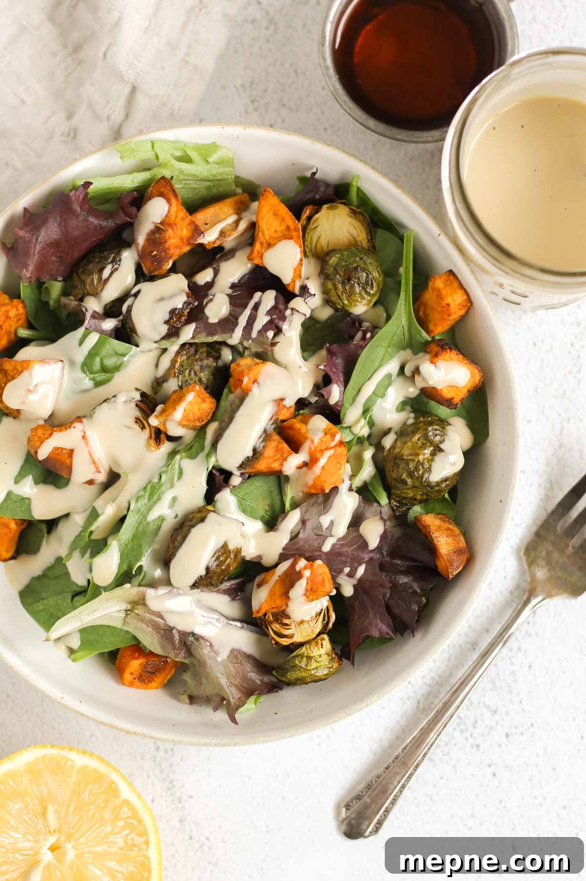 Creamy Maple Tahini Dressing for Salads and Grain Bowls 8 A bowl of greens and roasted veggies with maple tahini dressing drizzled over the top with a fork on the side of the bowl.