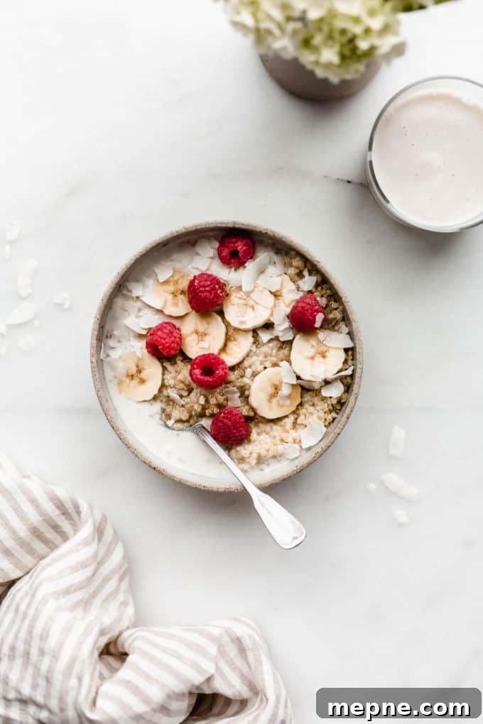 Protein-Packed Quinoa Breakfast Bowl with Avocado and Eggs 2 A breakfast quinoa bowl topped with bananas and berries with a glass of milk and flowers on the side