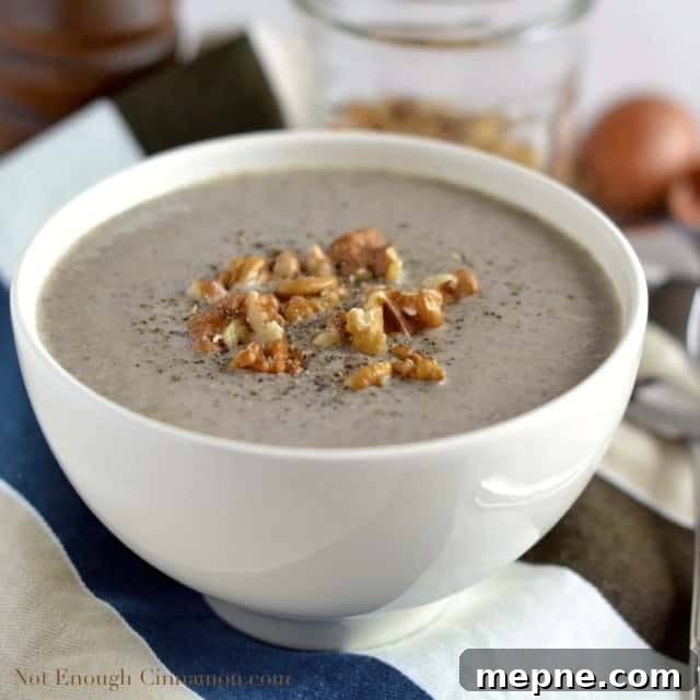 a white bowl of Skinny Cream of Mushroom Soup topped with chopped walnuts and freshly grated pepper