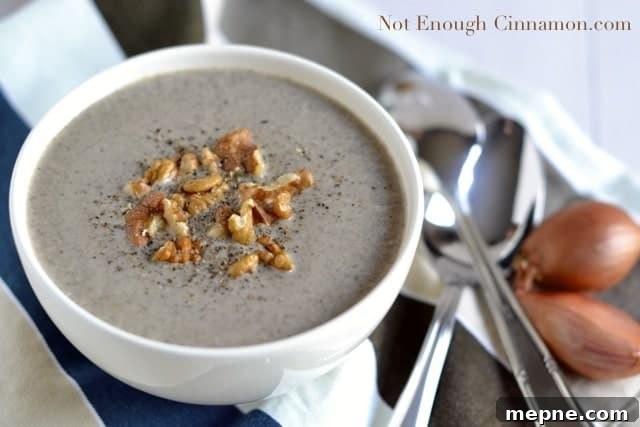 a white bowl of Skinny Cream of Mushroom Soup topped with chopped walnuts and freshly grated pepper with spoons and shallots on the side