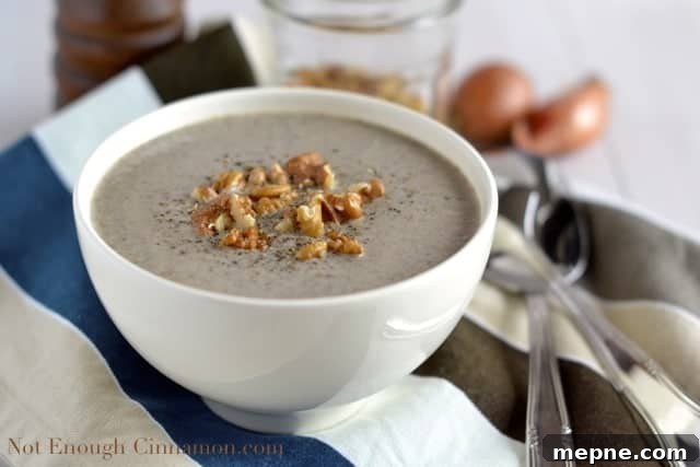 a white bowl of Skinny Cream of Mushroom Soup topped with chopped walnuts and freshly grated pepper