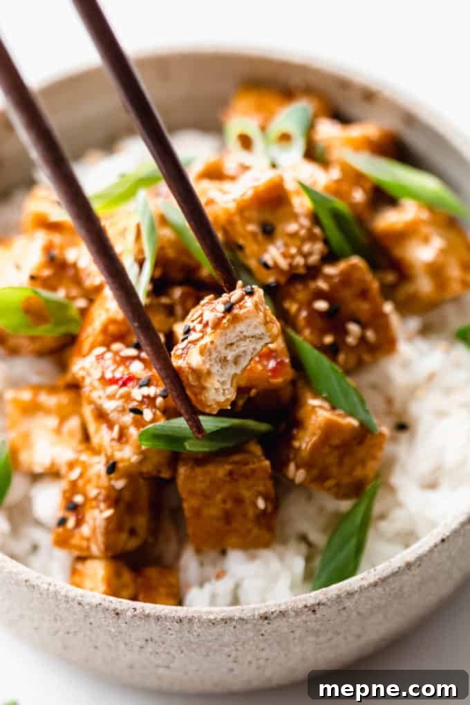 Crispy Baked Tofu with Teriyaki Glaze 8 chopsticks picking up a cube of teriyaki tofu