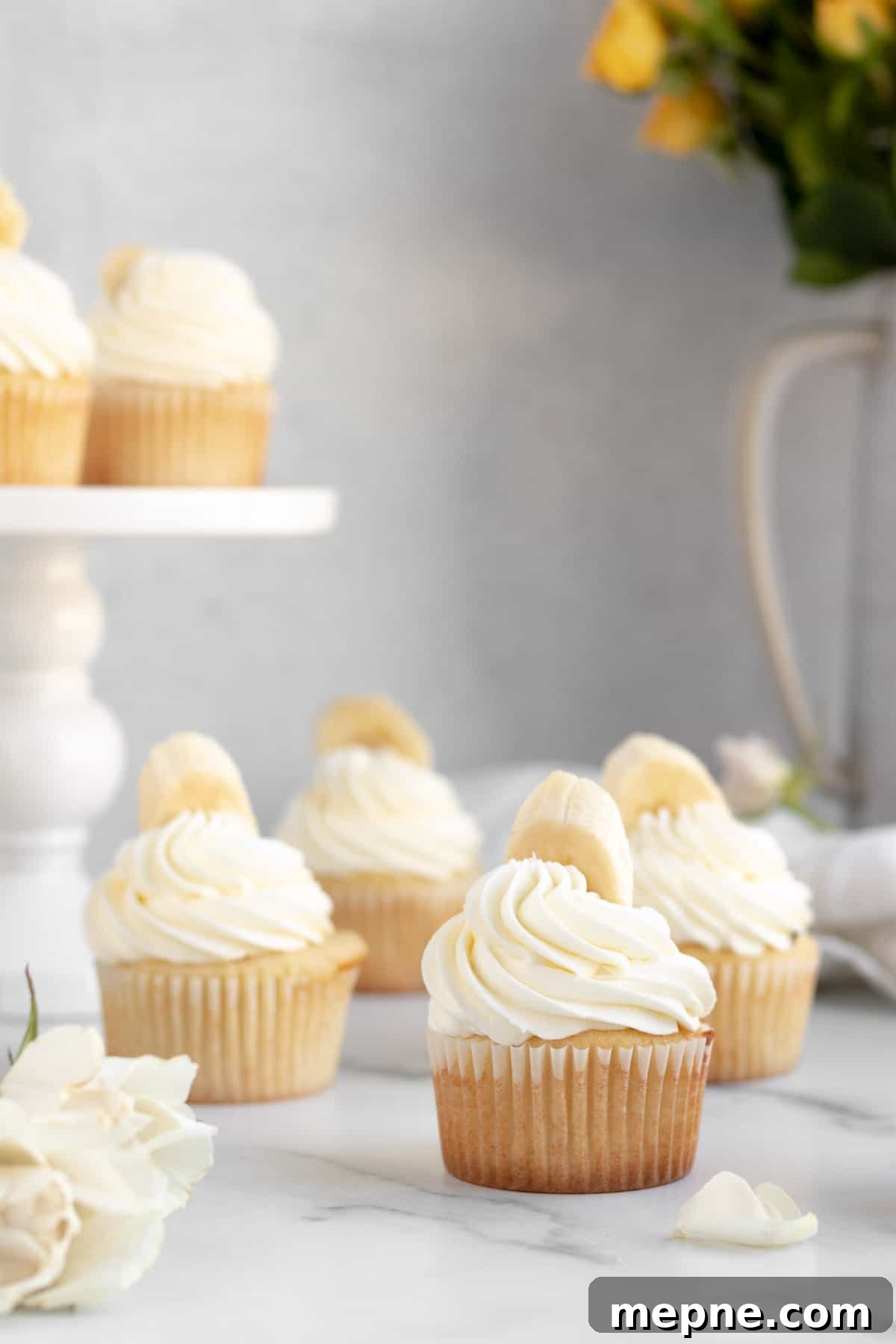 Creamy Banana Pudding Cupcakes with Vanilla Frosting 2 banana pudding cupcakes with white frosting and a banana on top sitting on a marble counter